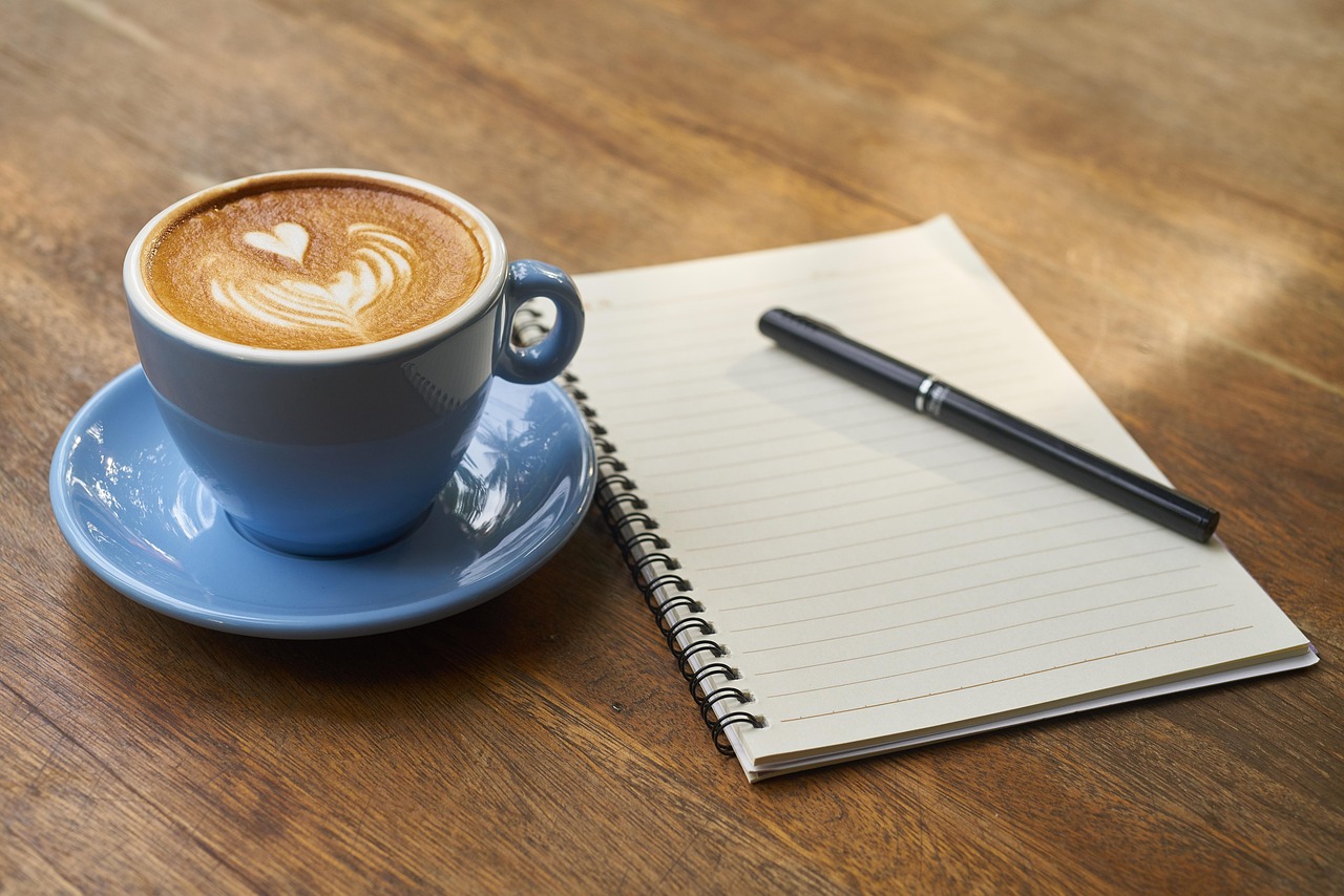 朝日が差し込む窓辺でノートとコーヒーを眺めながら、自分と向き合う時間を表したイメージ